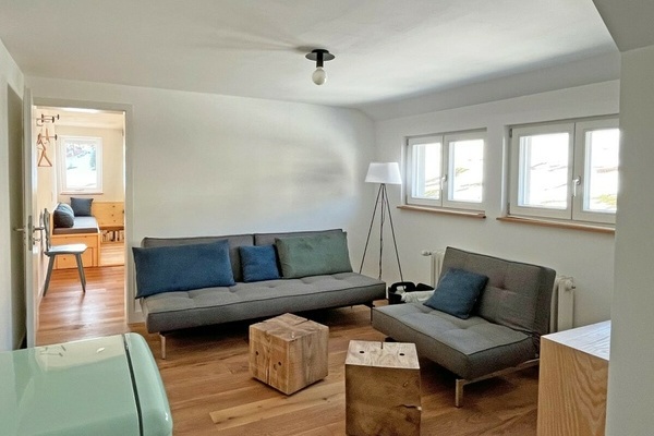Der Wohnraum  Eingang und Herz der Ferienwohnung. Offen, klar, ruhig, gemütlich. Mit Sofa und Sessel – beides lässt sich im Handumdrehen in ein bequemes Schlafsofa und eine Ottomane verwandeln. Zwei massive Würfel aus Tannenholz dienen als Hocker und / od